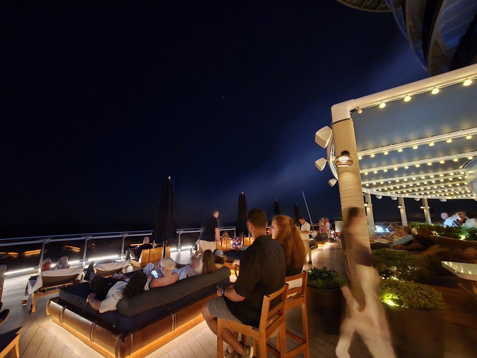 Guests relaxing on daybeds at The Dock during Stargazers on Virgin Voyages, at night